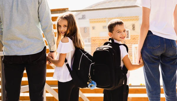 Two children hand in hand with their parents, with mother and father preparing to cross the threshold of the school on the first day of school. High quality photo