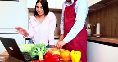 The woman answers the video call from the computer while the husband cuts vegetables. High quality 4k footage
