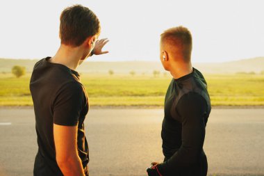 Back view of 2 sports man in black t-shirt talking about sports, one of them showing the other the route. High quality photo