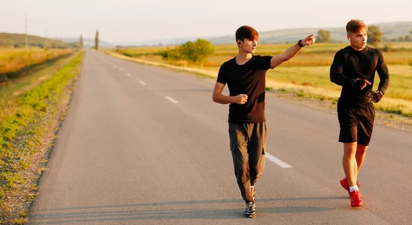 The happy friends running on the road, one of them shows the other the beautiful view from where the sun rises. High quality photo