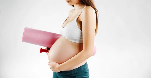 Pregnant woman holding a pink yoga mat and caresses his belly. High quality photo