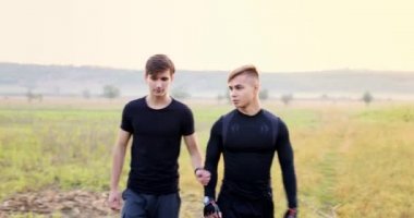 Two male friends talking while hiking together in the field. The man on the left then looks at the smart watch that tells him how many steps he has taken. High quality 4k footage