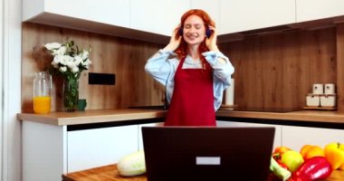 Pretty curly haired student wearing pajamas dancing in the kitchen while using headphones and listening to music. High quality 4k footage