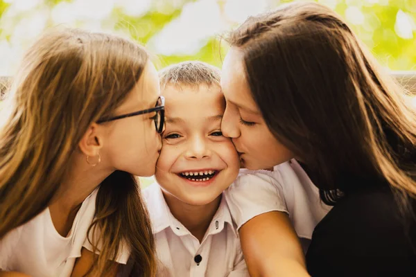 The older sisters kiss their younger brother who is very happy in first day of school. High quality photo