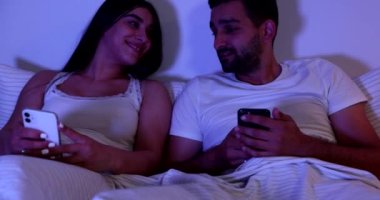 Bir erkek ve bir kadın, genç bir çift yatağa girmeden önce akıllı telefon kullanır ve birbirlerine bir şeyler gösterirler. Yüksek kalite 4k görüntü