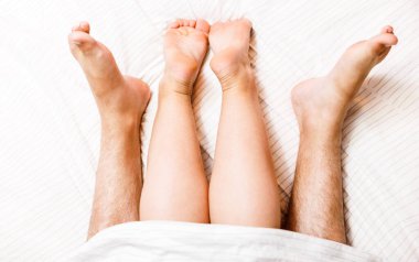 Yatakta tutkulu genç çift ilişkisi. İki partnerin de bacakları yorganın altından çıkıyor. Yüksek kalite fotoğraf