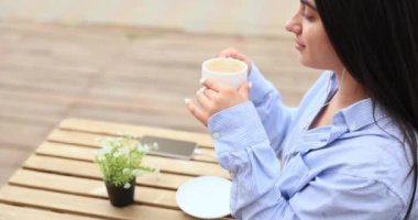 Kahverengi saçlı, mavi gözlü, kahve fincanı tutan ve dışarıda içki içen genç beyaz kızın portresi. Yüksek kalite 4k görüntü