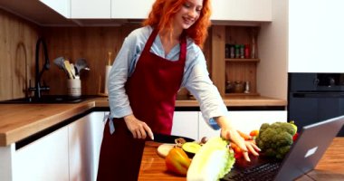 Salata için sebzeleri keserken, kızıl saçlı kız bilgisayardan gelen video çağrısına cevap verir. Yüksek kalite 4k görüntü