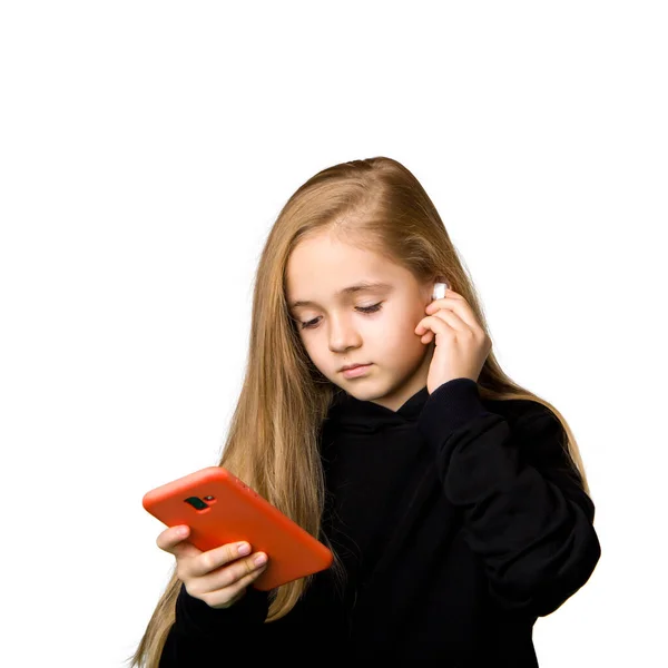 一个穿着黑色夹克的女孩拿着一部红色手机 并安装了无线耳机 与白种人隔离 — 图库照片