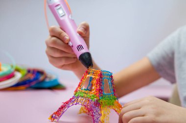 Çocuk 3 boyutlu bir kalem tutuyor ve renkli bir kule oluşturuyor..
