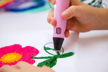 Çocuk 3 boyutlu bir kalem tutuyor ve çiziyor..