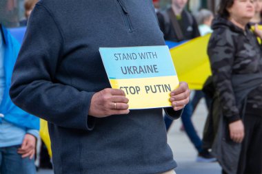 Bir adam Ukrayna bayrağı ve Ukrayna dur putin yazılı bir levha tutuyor.