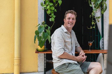 Neşeli bir adam pencerede yeşil çimlerle kokteyl barının önünde rahatlıyor ve Lizbon, Portekiz 'de bir bardaktan içiyor..