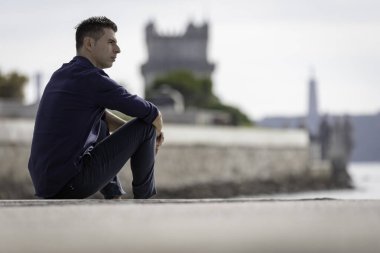 Portekiz 'de Lizbon nehri kıyısında tek başına dinlenen klas bir girişimcinin portresi. Şık bir iş adamı mavi şık bir gömlek ve resmi bir kıyafet giyiyor. Başarılı yaşam tarzı kavramı.