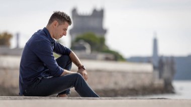 Portekiz 'de Lizbon nehri kıyısında tek başına dinlenen klas bir girişimcinin portresi. Şık bir iş adamı mavi şık bir gömlek ve resmi bir kıyafet giyiyor. Başarılı yaşam tarzı kavramı.