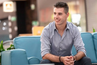 Portekiz 'de Lizbon' daki bir alışveriş merkezindeki mavi bir koltukta oturan serbest çalışan genç ve çekici bir mimar. Dünya çapında çalışan zarif elbiseli, gülümseyen genç adam..