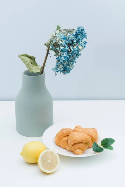 A vase with dried flowers and a plate of croissants