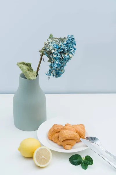 A vase with dried flowers and a plate of croissants