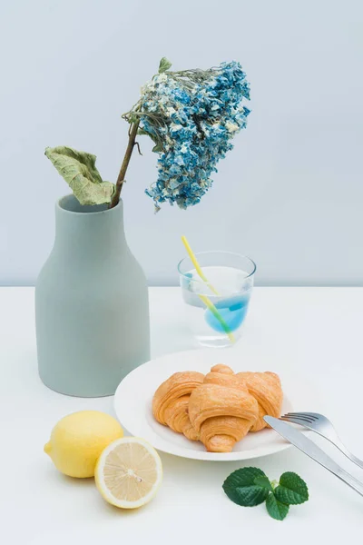 A vase with dried flowers and a plate of croissants
