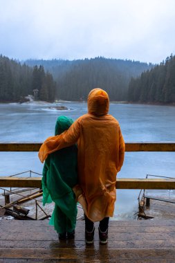 Yağmurluk giymiş iki çocuk buzla kaplı Synevyr Gölü 'nün keyfini çıkarıyor, Karpat Dağları, Ukrayna