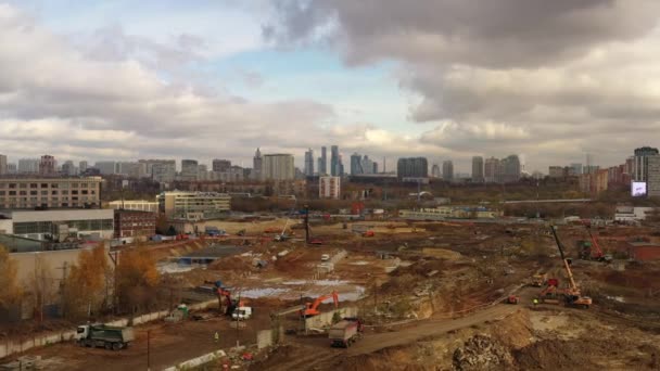 Luftaufnahme eines riesigen Moskauer Gebiets, in dem viele Baumaschinen arbeiten, und im Hintergrund sieht man Wolkenkratzer und graue Wolken — Stockvideo