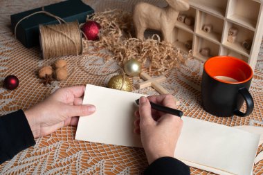 Noel tatili için hazırlık. Kadınların elleri masa üzerinde süslemeli kalem ve metin için boş kartlar tutuyor.