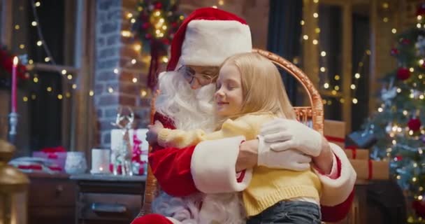 Ich liebe den Weihnachtsmann. Porträtansicht des hübschen Mädchens, das den Weihnachtsmann umarmt, während er auf seinen Knien sitzt. Urlaubskonzept — Stockvideo