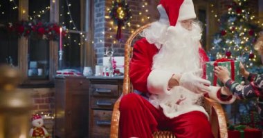 Vay canına. Küçük beyaz çocuk Noel Baba 'ya zevk duygularıyla hediye veriyor. Arka planda kürk ağacı ve yeni yıl süslemeleri
