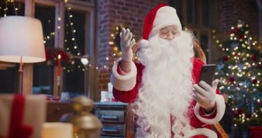 Hoş geldiniz. Neşeli sakallı Noel Baba koltukta oturup akıllı telefondaki video konuşmalarıyla etrafta bir sürü Noel hediyesi ve hediye kutusuyla sohbet ediyor. Tatil ruhu kavramı