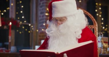 Noel Baba kitap okurken arka planda yeni yıl süslemeleri olan hediyelerle koltukta oturuyor. Tatil ruhu kavramı