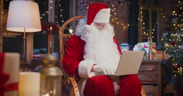 Sluiten van gelukkige senior man in kerstman kostuum typen op de laptop terwijl thuis zitten. Vakantieconcept — Stockvideo