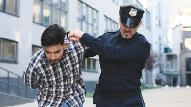 Vista de la cintura hacia arriba del retrato del policía esposando al joven caucásico y yendo con él al patrullero. Concepto criminal — Vídeos de Stock