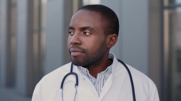 Visão retrato do médico multirracial alegre vestindo vestido de proteção em pé na rua perto do hospital e sorrindo para a câmera enquanto posando — Vídeo de Stock