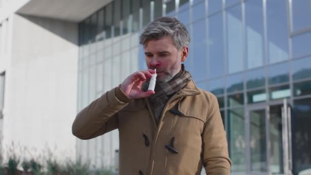 Homem sênior usando cachecol xadrez pulverizando spray nasal enquanto estava na rua da cidade. Conceito de terapia de saúde e medicina — Vídeo de Stock