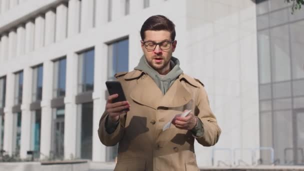 Een zieke blanke die niest op de achtergrond van de stad. Ill man met verkoudheid symptomen niezen buiten tijdens het gebruik van de smartphone. Portret van de man die lijdt aan allergie en zich slecht voelt — Stockvideo