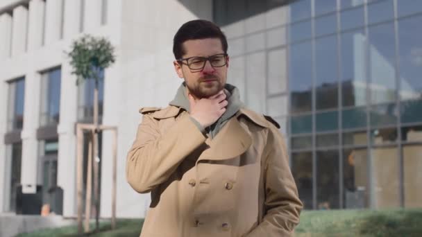 Close up portrait of unwell caucasian man standing at the street and covering mouth with hand while coughing and feeling sore throat. Virus infection concept — Stock Video