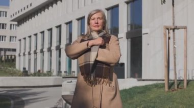 Sıcak atkıyı saran ve sokakta poz verirken kameraya gülümseyen pozitif yaşlı kadın. Sonbahar konsepti