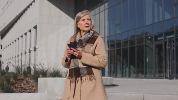 Cintura para arriba de mujer madura tosiendo en la calle de la ciudad. Retrato de mujer enferma de mediana edad de pie y usando su teléfono inteligente al aire libre — Vídeos de Stock