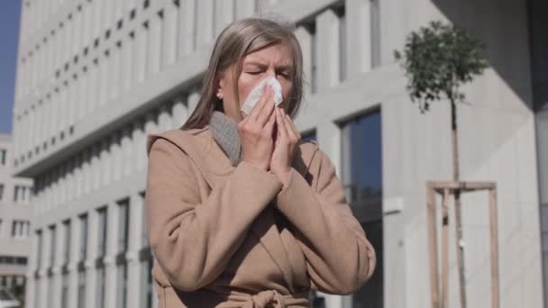 Mujer madura enferma parada al aire libre y tosiendo, estornudando. Retrato de una mujer enferma y hermosa que tose y tiene dolor en el pecho. Concepto de salud — Vídeos de Stock