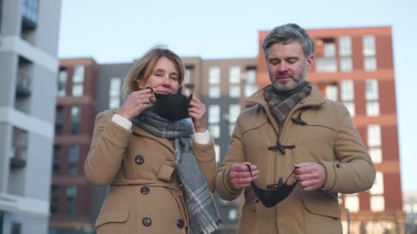 We beschermden ons leven. Bewegingscamera zicht van de Kaukasische senior paar nemen op beschermende maskers en glimlachen naar de camera terwijl het gevoel van veiligheid — Stockvideo