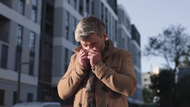 Porträt eines kaukasischen Mannes mit laufender Nase, der in der Stadt auf der Straße läuft und das Gesicht mit Gewebe bedeckt. Nahaufnahme von kranken, ungesunden Männern, die niesen und husten. Virenkonzept — Stockvideo