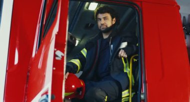 Özel elbiseli, kasklı, itfaiye arabasında oturan ve kameraya gülümseyen çekici beyaz bir sucu. İçeri gir. Portre.