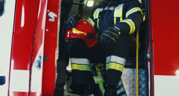 Portrait de l'homme d'eau afro-américain attrayant dans les vêtements spéciaux et avec un casque assis dans le coffre du feu et regardant avec un sourire à la caméra. À l'intérieur. — Video