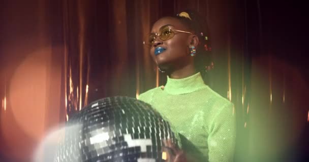Giovane donna afroamericana in top a rete verde e occhiali da sole gialli tiene palla disco e sorride. Ragazza felice con trucco audace gode di musica, divertirsi da solo alla festa. — Video Stock