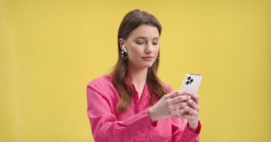 Kablosuz kulaklıkla müzik dinlerken dans eden, sarı arka plan duvarında gülümseyen, alet edevat kullanan, boş zaman kavramı kullanan oldukça mutlu genç bir kadının portresini kapat.