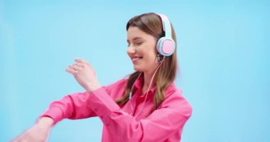 Neşeli beyaz kadın dans ederken, renkli kulaklıklarla müzik dinlerken ve gülümserken yakın plan portresi. Güzel mutlu kadın model mavi arka planda dans ediyor, pozitif duygular.