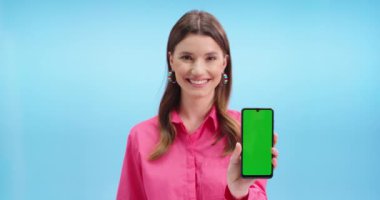 Krom anahtarla cep telefonunun kamerasına gülümseyen mutlu beyaz kadın modelin portresini yakından çek. Mavi duvarda duran yeşil ekranlı akıllı telefonu gösteren güzel bir kadın.