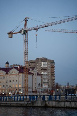 Büyük bir endüstriyel vinç tarafından yönetilen, mavi gökyüzüne karşı inşaat halindeki yüksek katlı bir bloğu olan bir inşaat alanı..