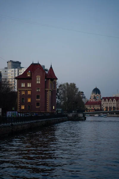 Alacakaranlıkta nehir kıyısındaki ışıktan parlayan pencereli tuğla ev