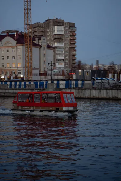 Turistler kırmızı bir teknede, geniş bir nehirde küçük tekneler. Nehirdeki katamaranlı insanlar şehrin arka planına karşı.